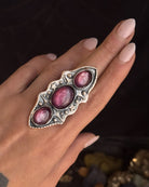 Silver ring with pink stones on a hand against a dark background