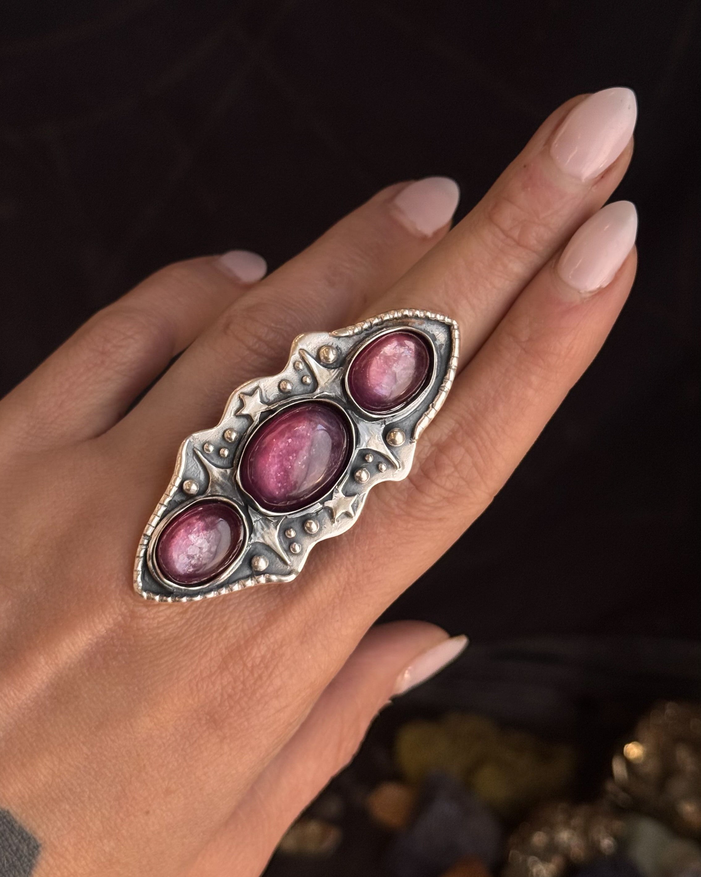 Silver ring with pink stones on a hand against a dark background
