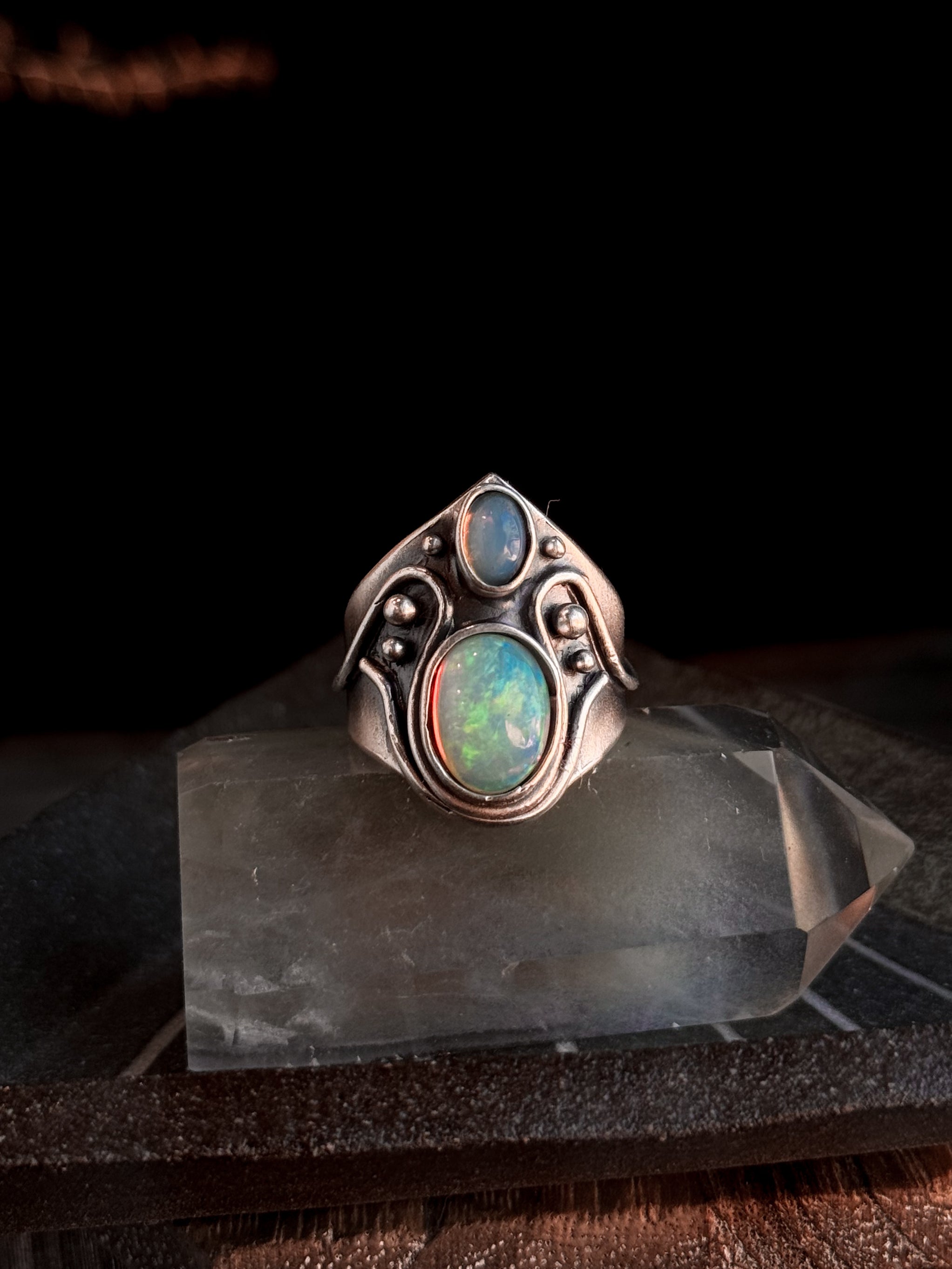 Silver ring with opal stones on a clear stand against a dark background