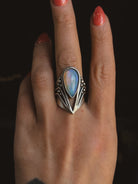 Hand wearing a silver ring with a blue stone against a dark background